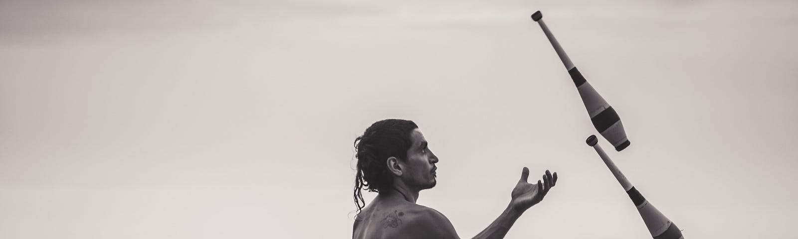 A black and white photo of a man juggling pins on a beach.