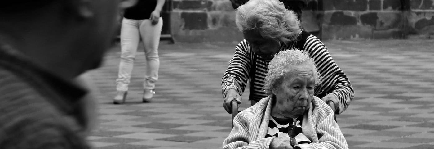 Black-and-white photo of a daughter pushing her mother in a wheelchair.