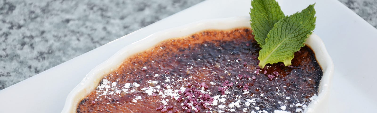 an enticing dish of creme brulee with a mint leaf garnish