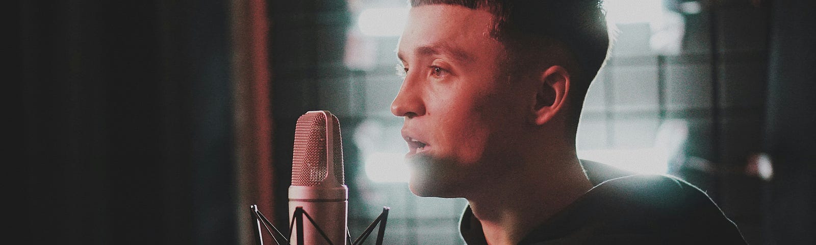 A person speaks or sings into a recording microphone in a dimly lit studio