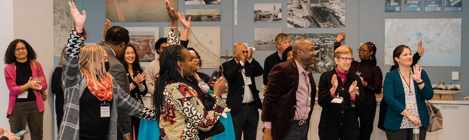 Candid photo of 1–2 dozen people standing in a museum wearing business clothes. They are smiling and raising the hands.