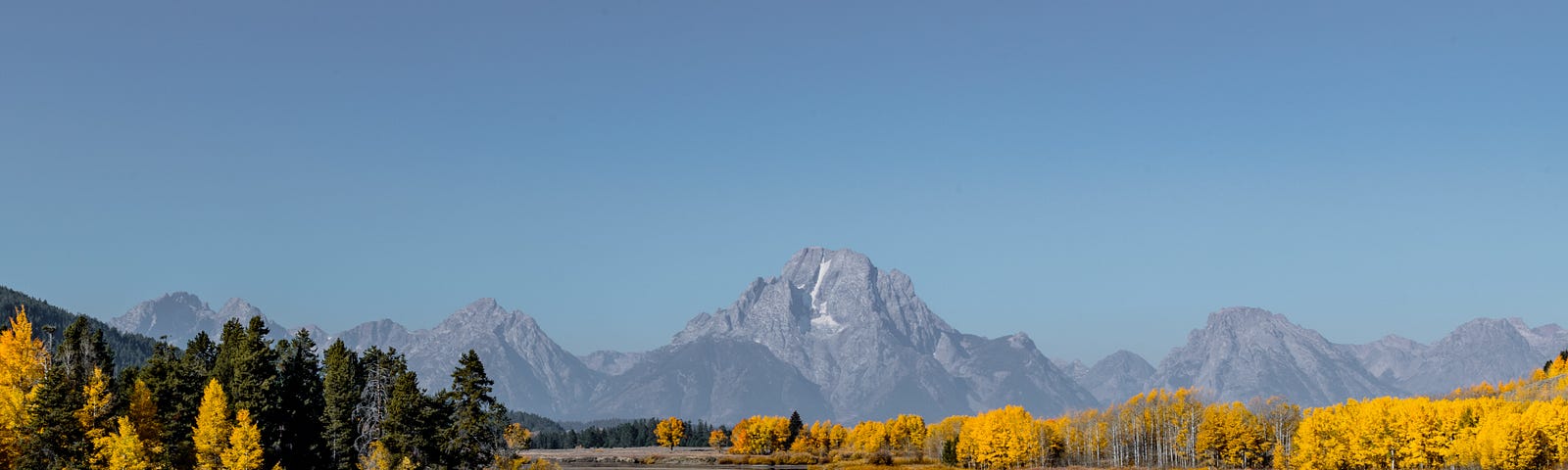 A Wyoming river, surrounded by fall colors of yellows, browns, and greens, with mountains in the distance