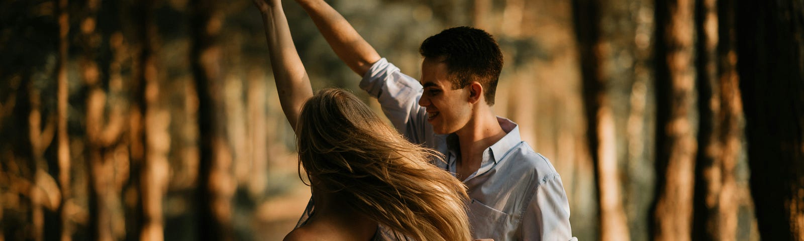 There are two lovers in a dancing pose amid a forest lane covered by several trees looking so much in love.