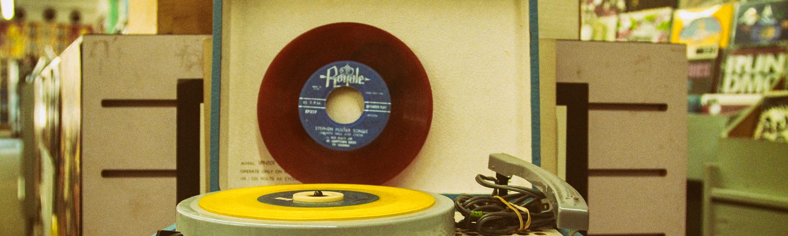 A vintage green record player with a yellow 45-record on it, ready to play