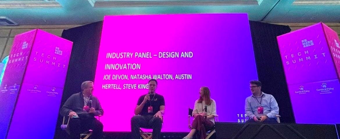 The four panel participants on stage in front of a pink and purple screen that reads “Industry Panel — Design and Innovation”