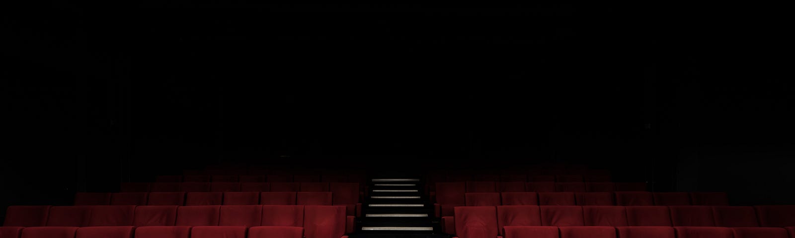 An empty movie theater with red seats and stairs in the middle. It suggests a screen ahead.