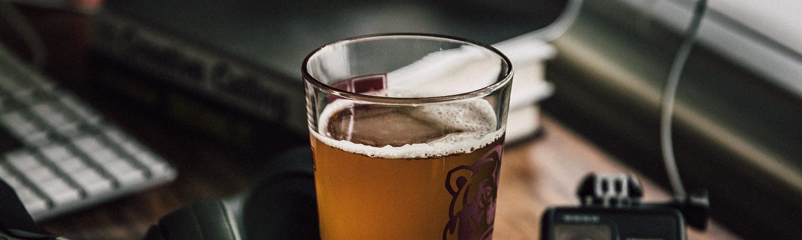 A glass of beer next to a keyboard and office equipment.