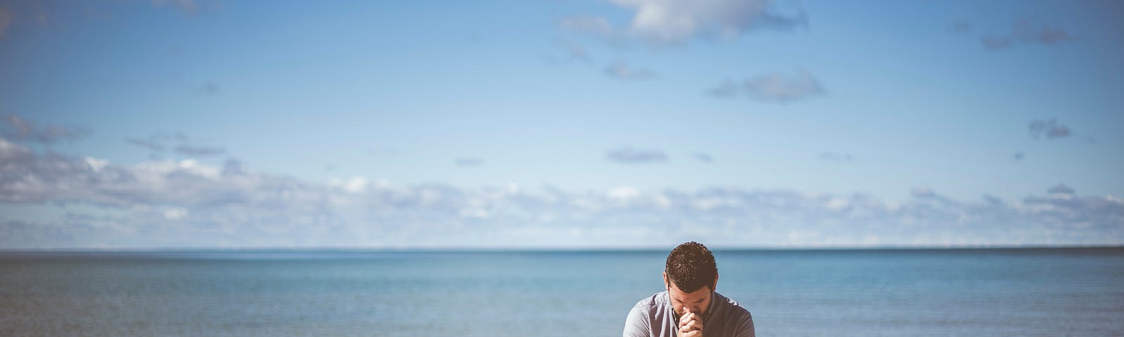 A man kneeling in prayer in front of a body of water.
