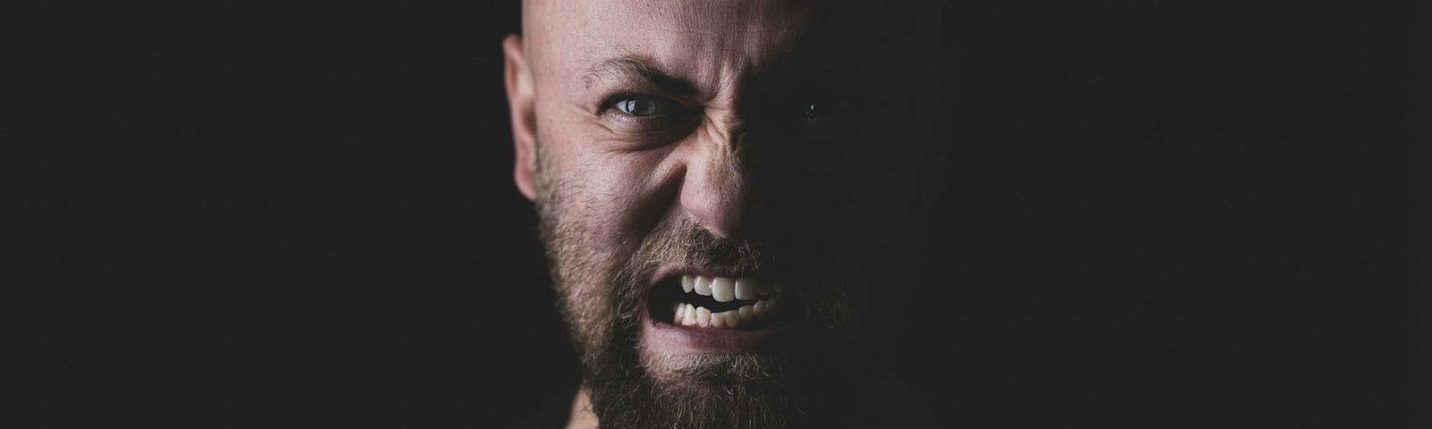The face of an angry man, against a black background.