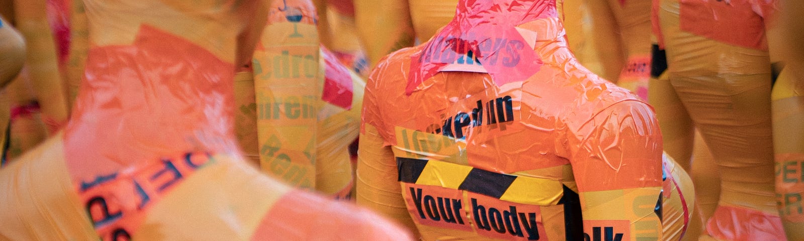 A bunch of mannequins with feminine bodies, all wrapped in tape, some with words, focused in particular on one that reads “your body belongs to you”