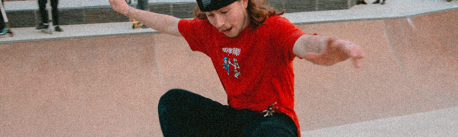 A young man in a red t shirt and toque, riding a rail on a skateboard