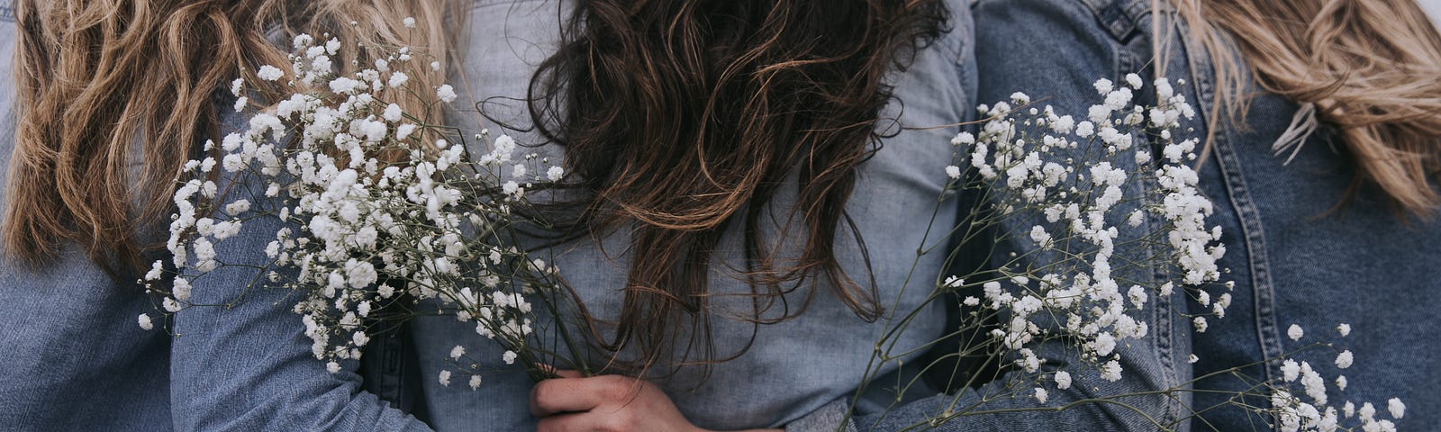 Three teenage girlfriends holding wild flowers