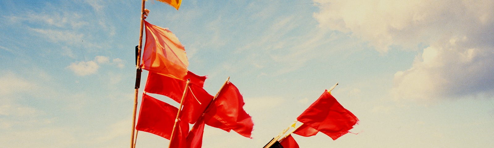 A small row boat sits on a beach with several red flags protruding from it at various angles.