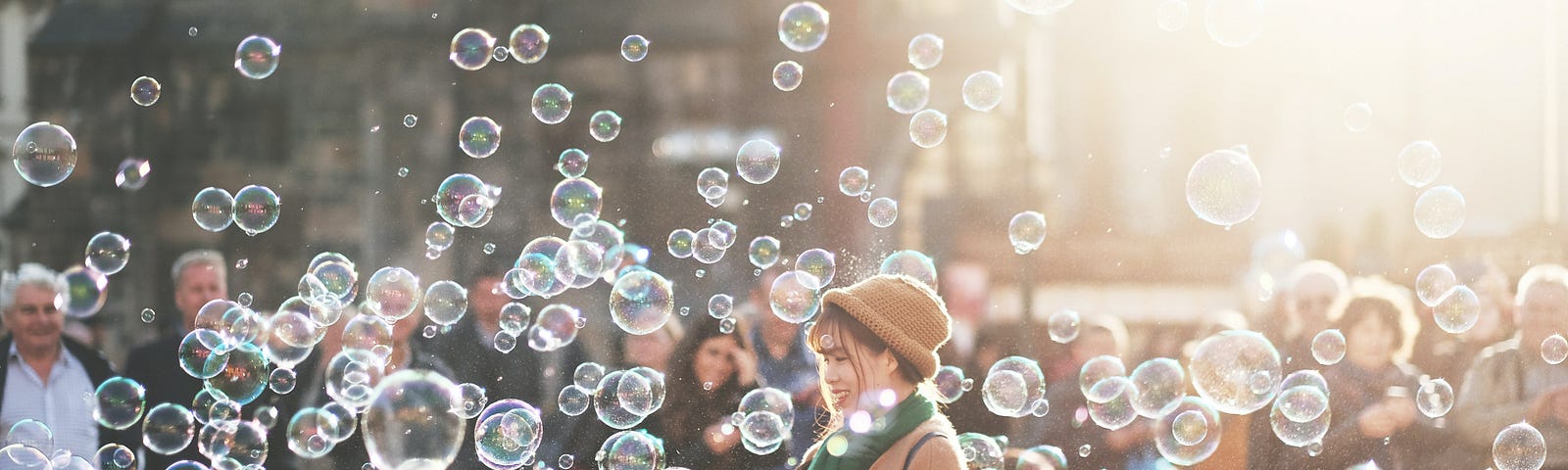 An Asian woman in the middle of a thousand soap bubbles of different sizes, while surrounded by a crowd of people, watching her.