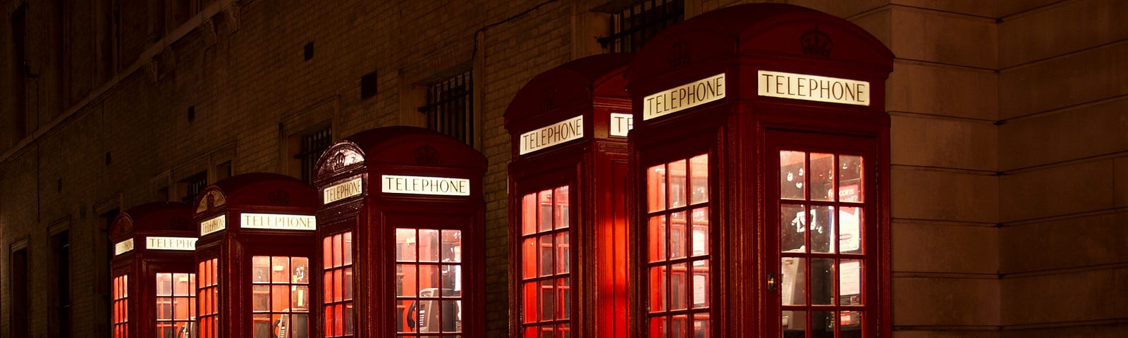 a line of red telephone booths against a wall; all are lit from the inside. They look like lanterns.