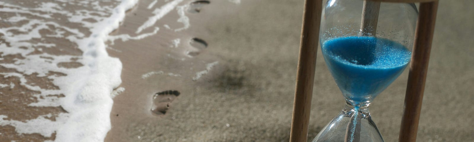 Hour glass with blue sand, sitting on the sea shore