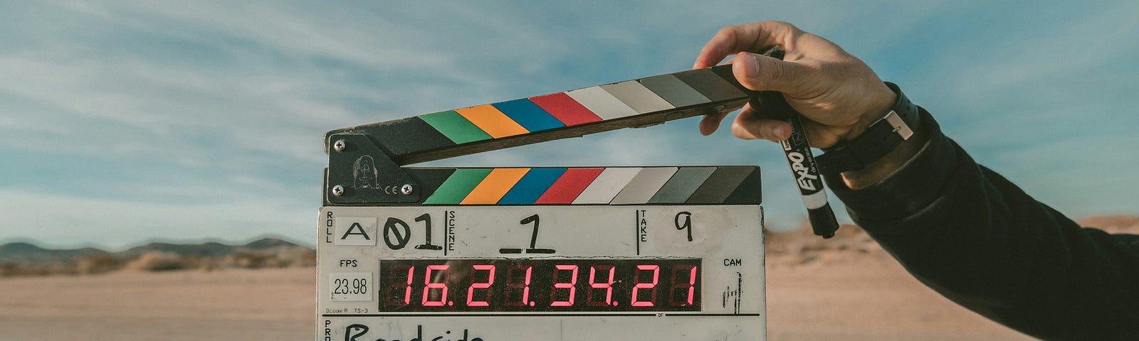 A clapperboard held up in front of flat ground with sand