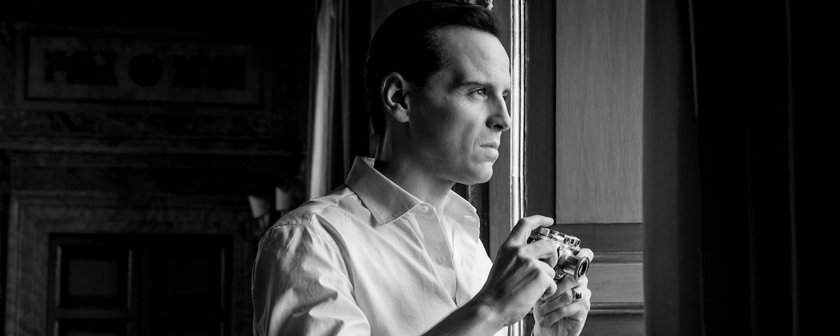 Photo shows a 47-year-old version of Tom Ripley, played by Andrew Scott, apparently wearing a wig and staring out a window in a crisp white cotton shirt, posing with an old 35mm camera.