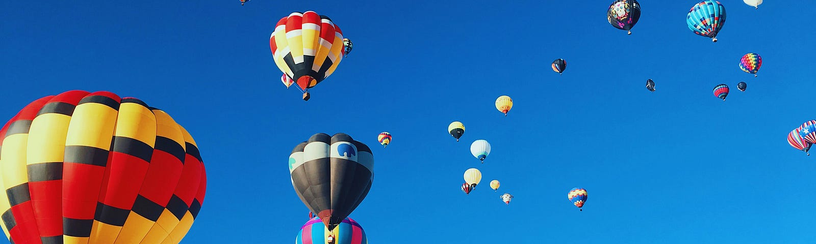 A beautiful blue sky filled with dozens of colorful hot air baloons in flight.