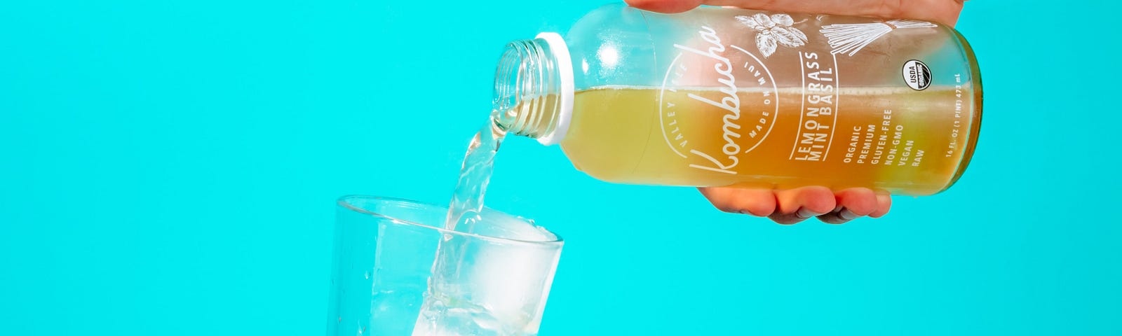A hand extends from the right to pour kombucha from a glass bottle into a drinking glass (with ice). Kombucha decreases blood sugar for those with type 2 diabetes.