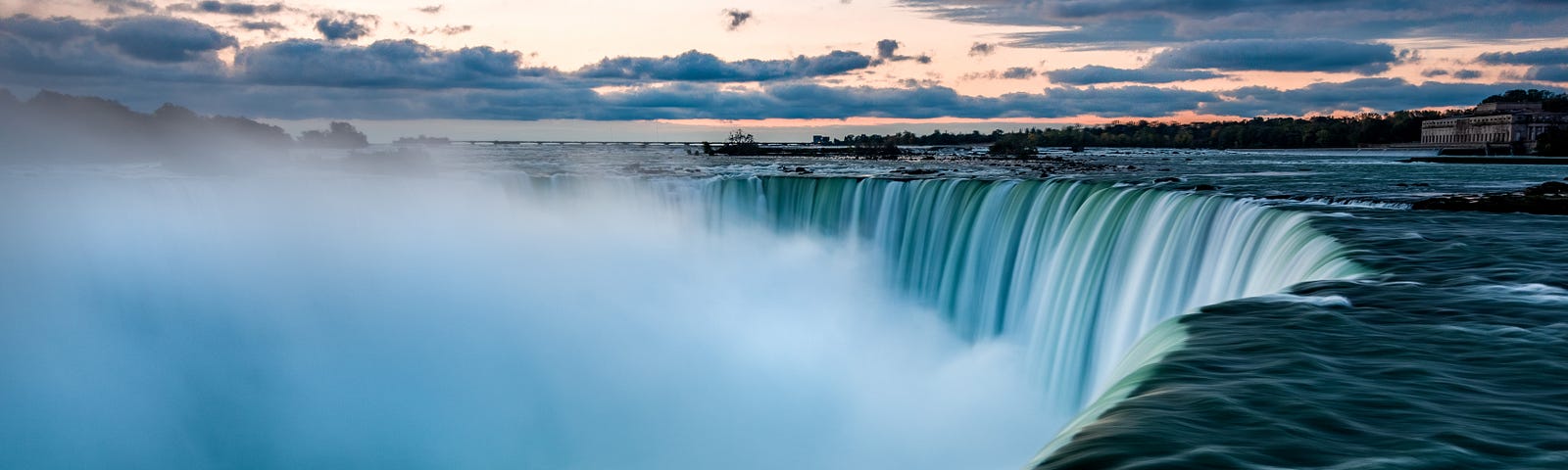 Niagara Falls from a side view. Deep blue water and cloudy skies.