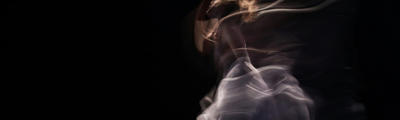 A blurry photograph of a woman dancing on a stage with a black background.