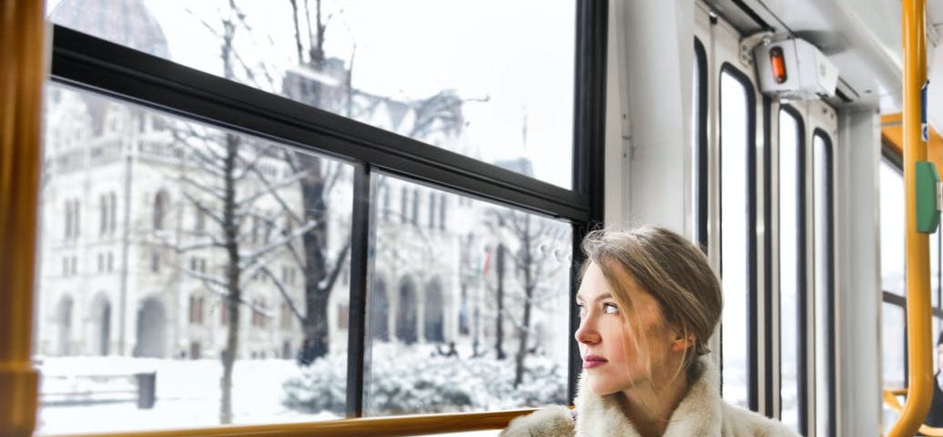Woman in a fur coat, looking out a window at a snowy scene.