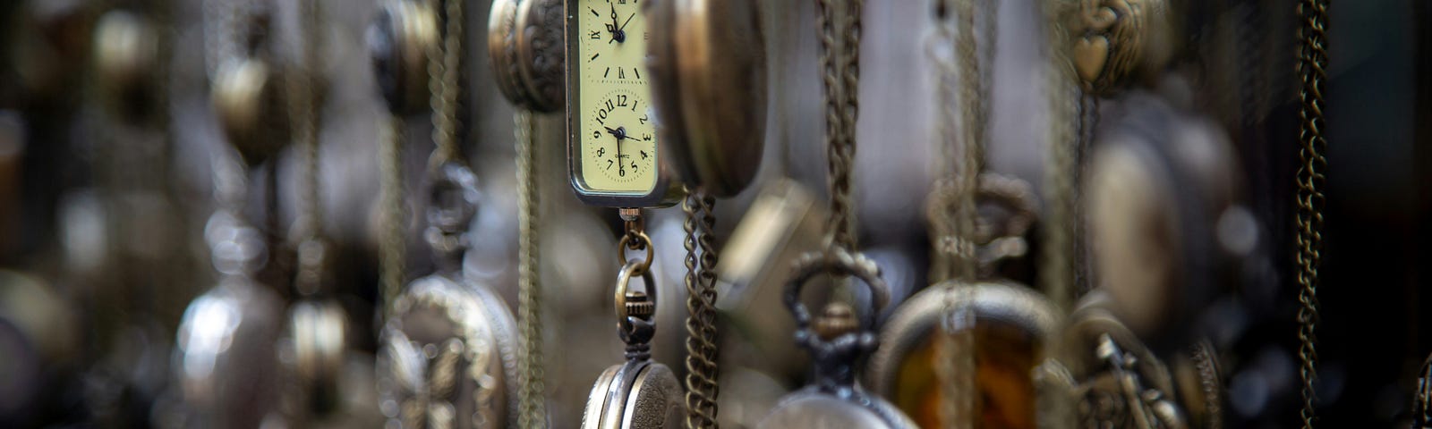 A photo of many antique pocket watches hanging on their chains. Photo by Alex Guillaume on Unsplash