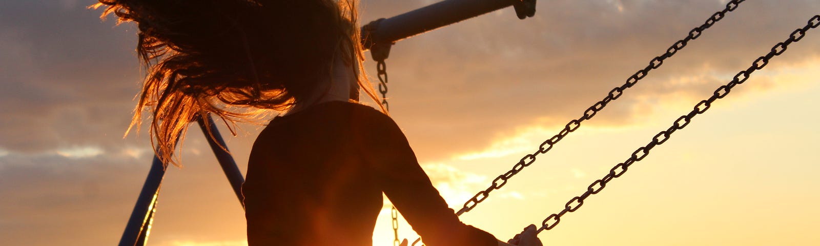Woman on a swing at a beach with the setting sun behind her.
