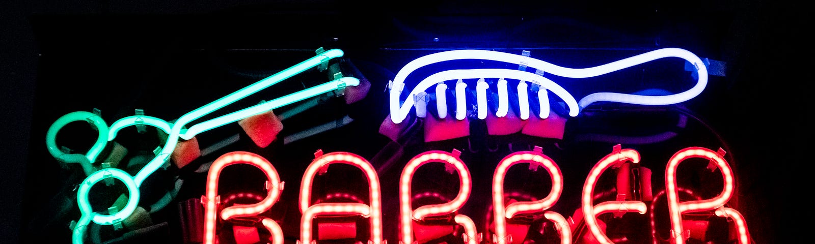 Neon sign with the word ‘barber’ in orange, a pink comb and green scissors.