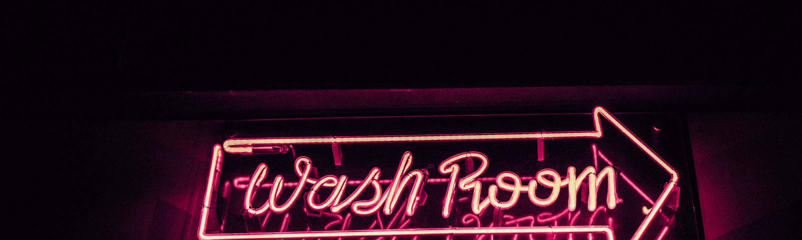 Photo of a neon sign of an arrow with the word Wash Room inside it.