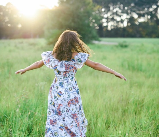 girl wearing flowered dress twirling in a field of green grass