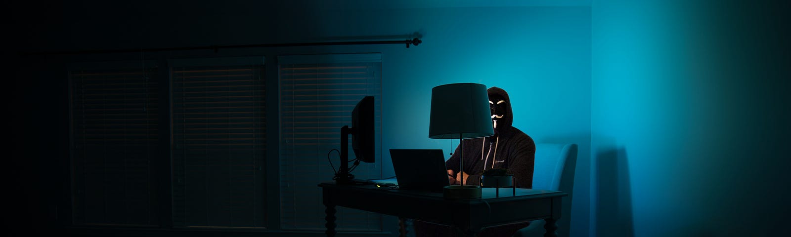 person in black ski mask sitting in front of a computer in a darkened room