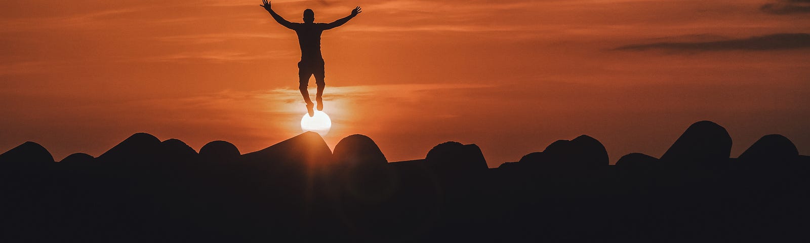man with open arms appearing to jump off sun at sunset