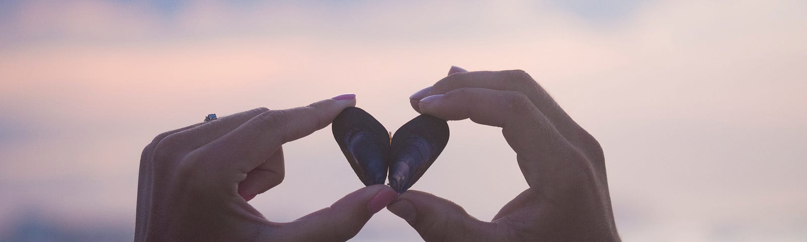 Two hands holding two pebbles forming a heart sign.