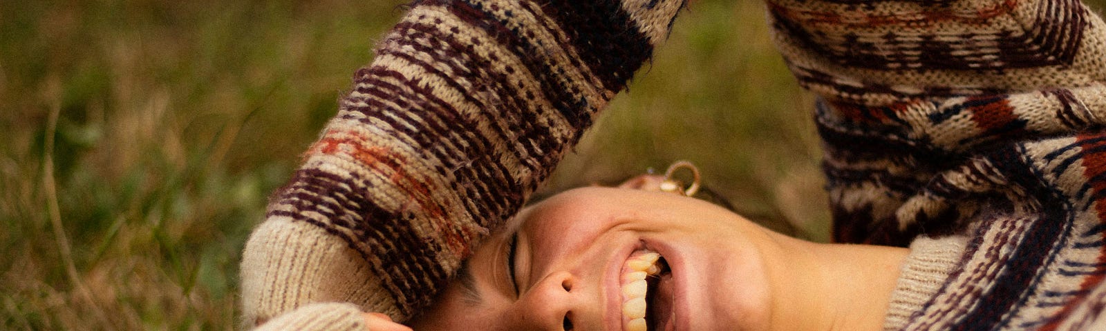 A woman laying in the grass, laughing.
