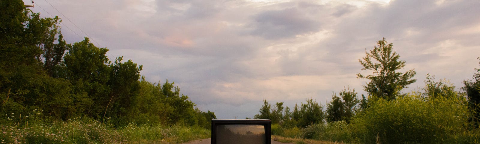 An old-fashioned television set sits abandoned in the middle of an empty country road