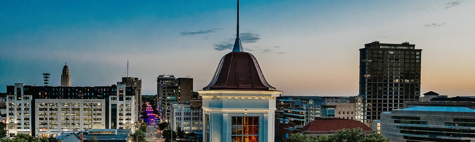 The sun sets on Lincoln with the Love Library cupola in the foreground and downtown Lincoln in the distance