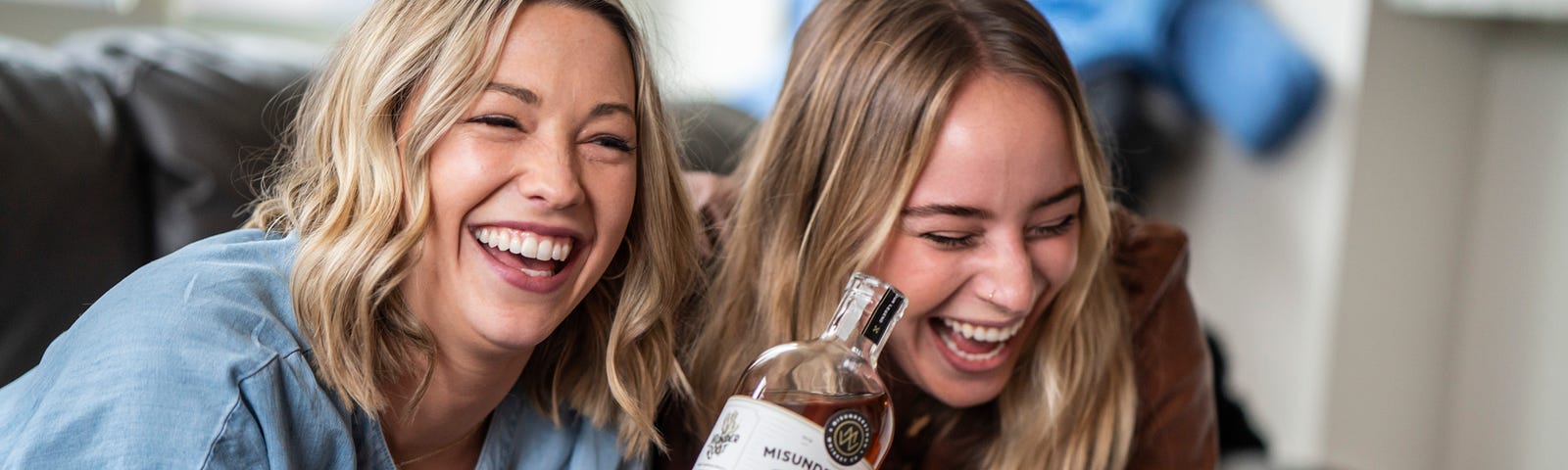 two pretty blonde girls laughing with a whiskey bottle.