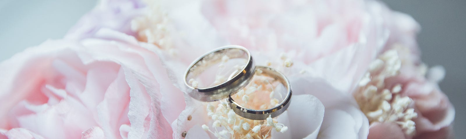 Two wedding rings, resting on top of a pink and white bouquet