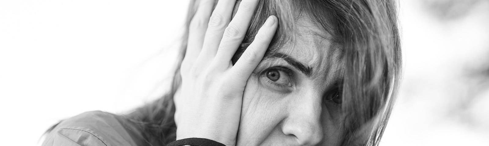 In black and white, a distressed woman clutches her hands to her face