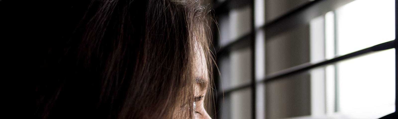 Woman staring out of the window through Venetian blinds