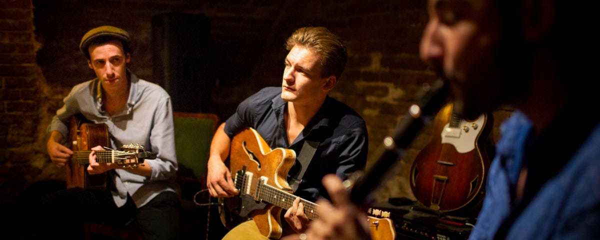 Two men playing guitar, one main playing an oboe.