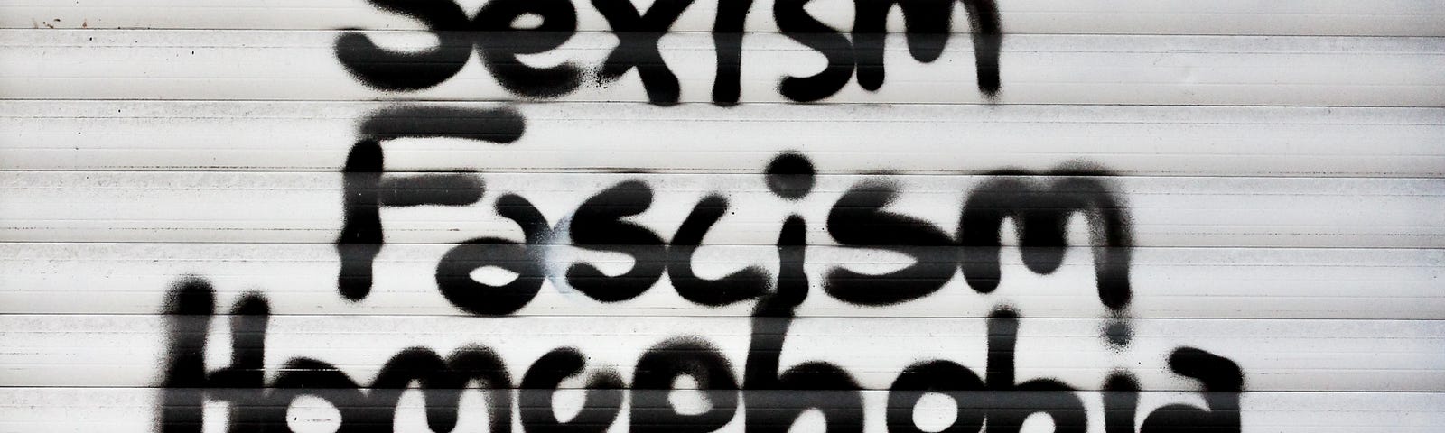 Graffiti spray painted onto a wall. “No place for: Racism, sexism, fascism, homophobia, transphobia, fatphobia or hate!”