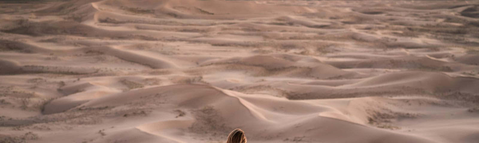 A women sitting in a desert, either at day break or dusk