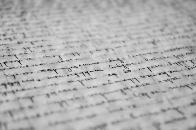 Blurred image (clear in line horizontal-centered) of cursive lyrics in blank ink written on faint-lined paper