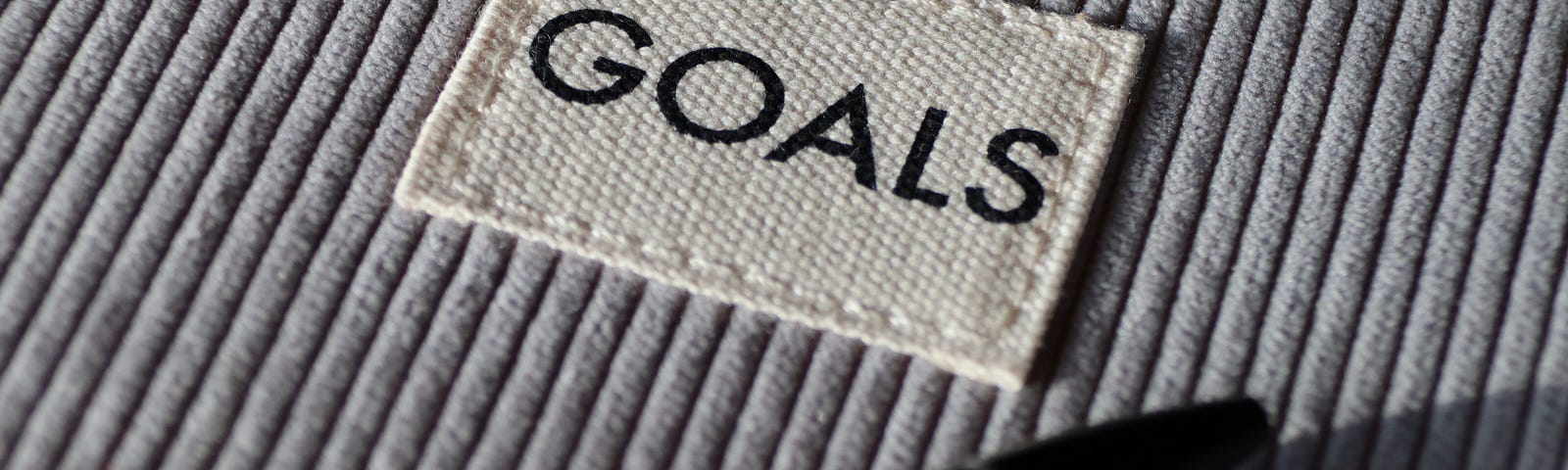 Grey corduroy fabric with the word goals sewn on a patch and a pen on the fabric