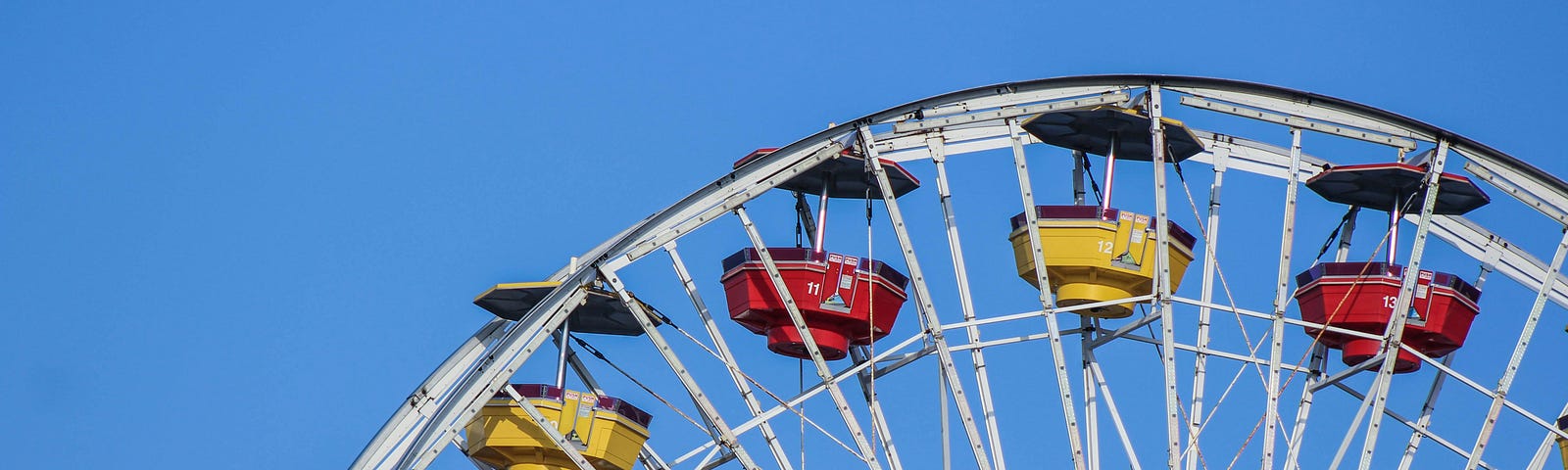The arch of a Ferris Wheel, compartments raised to the clear blue sky, suspends tiny passengers.