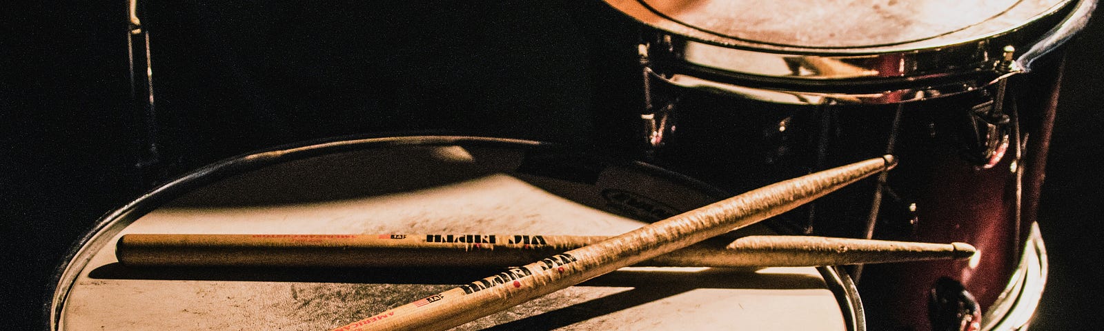 A well-worn drum set with a pair of drumsticks resting on it.