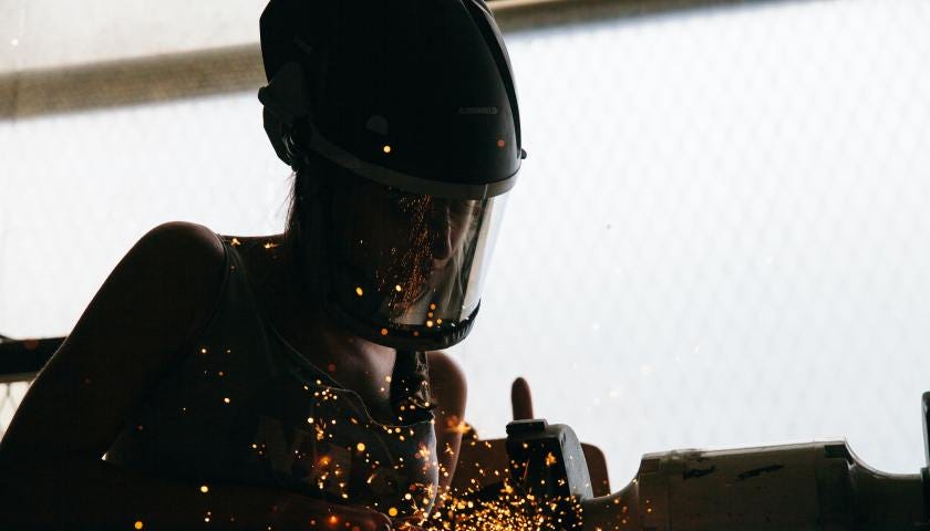 A worker welds parts together while manufacturing machine parts.